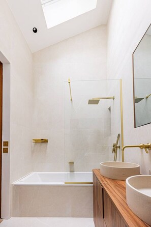 Ein modernes Badezimmer mit einer großen Badewanne, zwei Waschbecken und einer Duschkabine aus Glas.