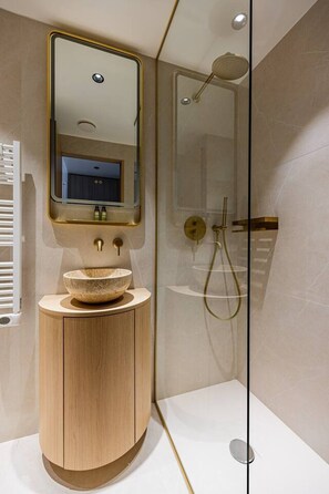 Ein modernes Badezimmer mit einem Holzbettchen, einem runden Waschbecken, einem Spiegel und einer gläsernen Duschkabine.