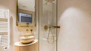 Un baño moderno con un lavabo de piedra, cabina de ducha de vidrio y un espejo sobre el lavabo.