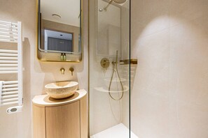 Ein modernes Badezimmer mit einem Steinsink, einer Duschkabine aus Glas und einem Spiegel über dem Waschbecken.