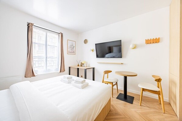 Ein Hotelzimmer mit Bett, Fernseher, kleinem Tisch, zwei Stühlen und einem Fenster mit Vorhängen.