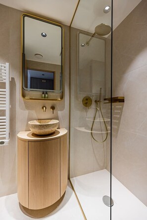 Ein modernes Badezimmer mit einem Holzbadschrank, einem runden Waschbecken, einem Spiegel und einer Duschkabine aus Glas.