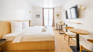 Una habitación de hotel con cama, escritorio, silla, televisor y ventana con cortinas.