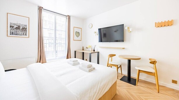 Una habitación de hotel con cama, escritorio, silla, televisor y ventana con cortinas.