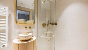 Un baño moderno con un lavamanos independiente, un box de ducha con mampara de vidrio y un espejo con marco dorado.