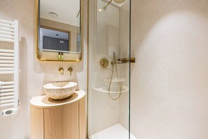 Ein modernes Badezimmer mit freistehender Waschtasche, einer Duschkabine aus Glas und einem Spiegel mit Goldrahmen.