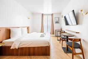 Ein Hotelzimmer mit einem Bett, einem Schreibtisch, einem Sessel, einem Fernseher und einem Fenster mit Vorhängen.