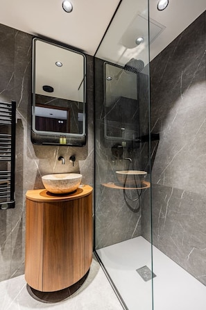Ein modernes Badezimmer mit einem Holzbettchen, einem großen Spiegel und einer Duschkabine aus Glas.