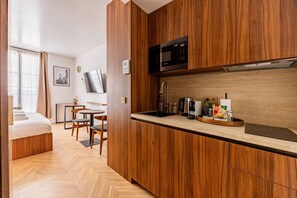 Ein kompaktes Hotelzimmer mit Küchenzeile, einem Bett, einem Essbereich und einem Fernseher.