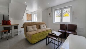 Een moderne woonkamer met een bank, een bijzettafeltje, een stoel en een raam met uitzicht op bomen.