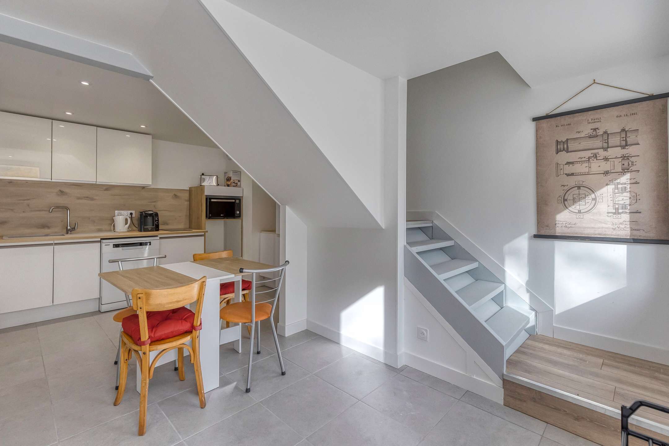 Een moderne keuken met witte kasten, een houten eettafel en een trap met een lichte houttint.