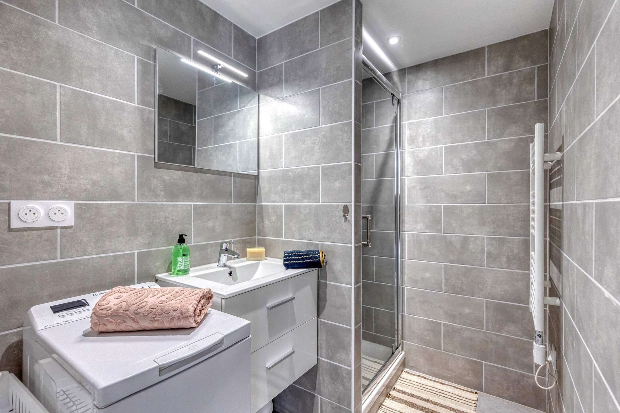 A modern bathroom with a shower, a sink, a mirror, and a towel.