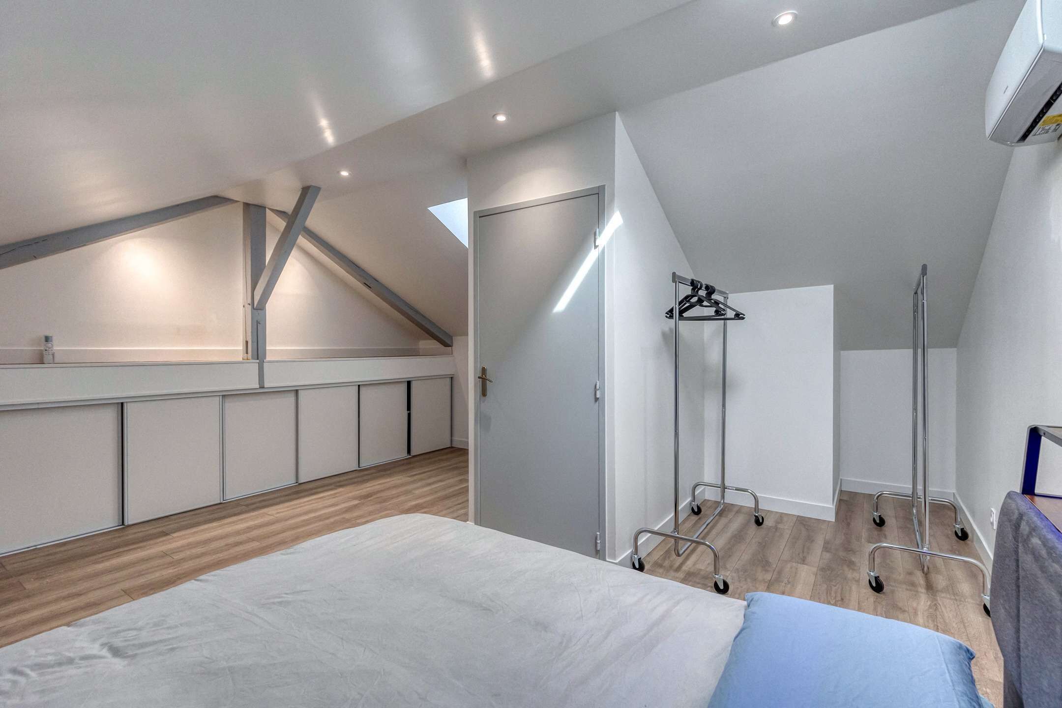 Un dormitorio moderno con techo inclinado, una cama con almohada azul, un armario y un vestidor.