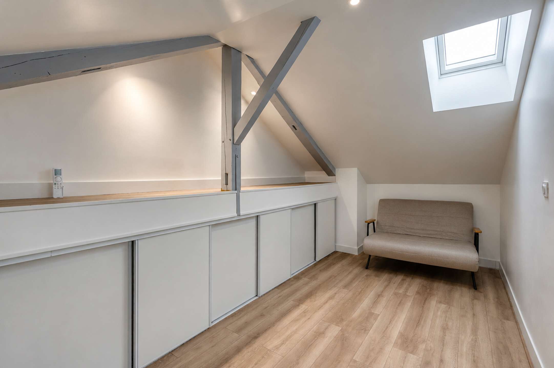 A modern loft bedroom with a sloped ceiling, a built-in bench, and a skylight.