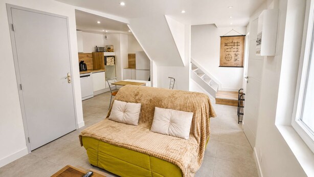 Een kamer met een bed, een keuken op de achtergrond en een trap naar een ander niveau.