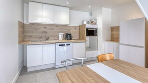 Een praktische keuken met witte kastjes, een houten aanrechtblad, een vaatwasser, een magnetron en een eethoek met een tafel en stoelen.