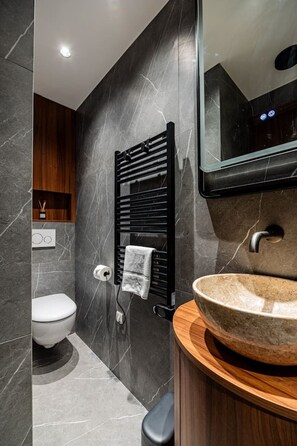 Ein modernes Badezimmer mit Marmorwand, einem schwarzen Handtuchwärmer, einem runden Waschbecken und einer Toilette.