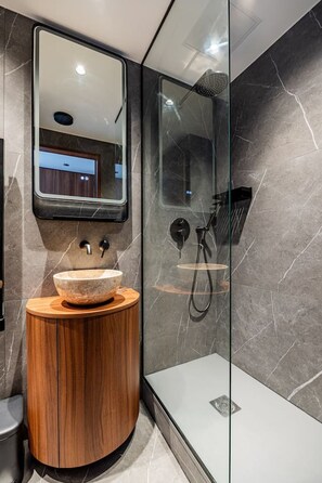 Ein modernes Badezimmer mit einem Holzkosmetikschrank, einem großen Spiegel, einer Duschkabine und Marmorwänden.