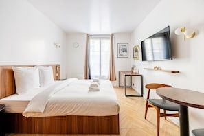 Ein Hotelzimmer mit Bett, Schreibtisch, Sessel, Fernseher und Fenster.