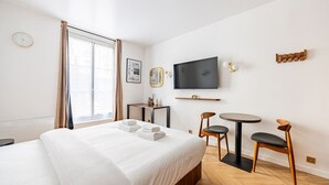 A hotel room with a bed, a TV, a small table, two chairs, and a window with curtains. - 151. Luxury suite-Etienne Marcel-Châtelet-Paris 3 (Paris)