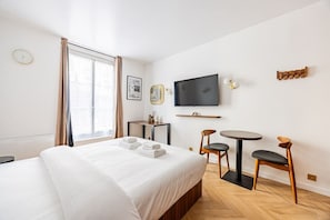 Ein Hotelzimmer mit einem Bett, einem Fernseher, einem kleinen Tisch, zwei Stühlen und einem Fenster mit Vorhängen.