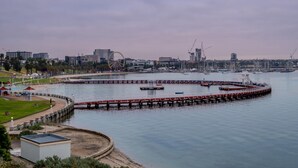 Blick auf das Wasser mit einer anlegenden Mole, einer entfernten Skyline und einem klaren Himmel.