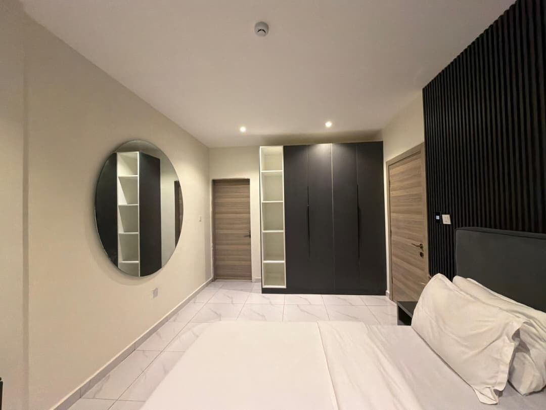 Una camera da letto moderna con un letto, uno specchio rotondo, armadi a muro e un'ampia finestra.