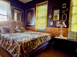 Ein Schlafzimmer mit einem Bett, einem Nachttisch, einem Spiegel und Wandbildern.