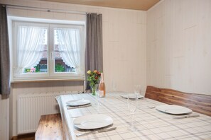 Een eettafel gedekt met borden, bestek en glazen, een vaas met bloemen en een raam met gordijnen.