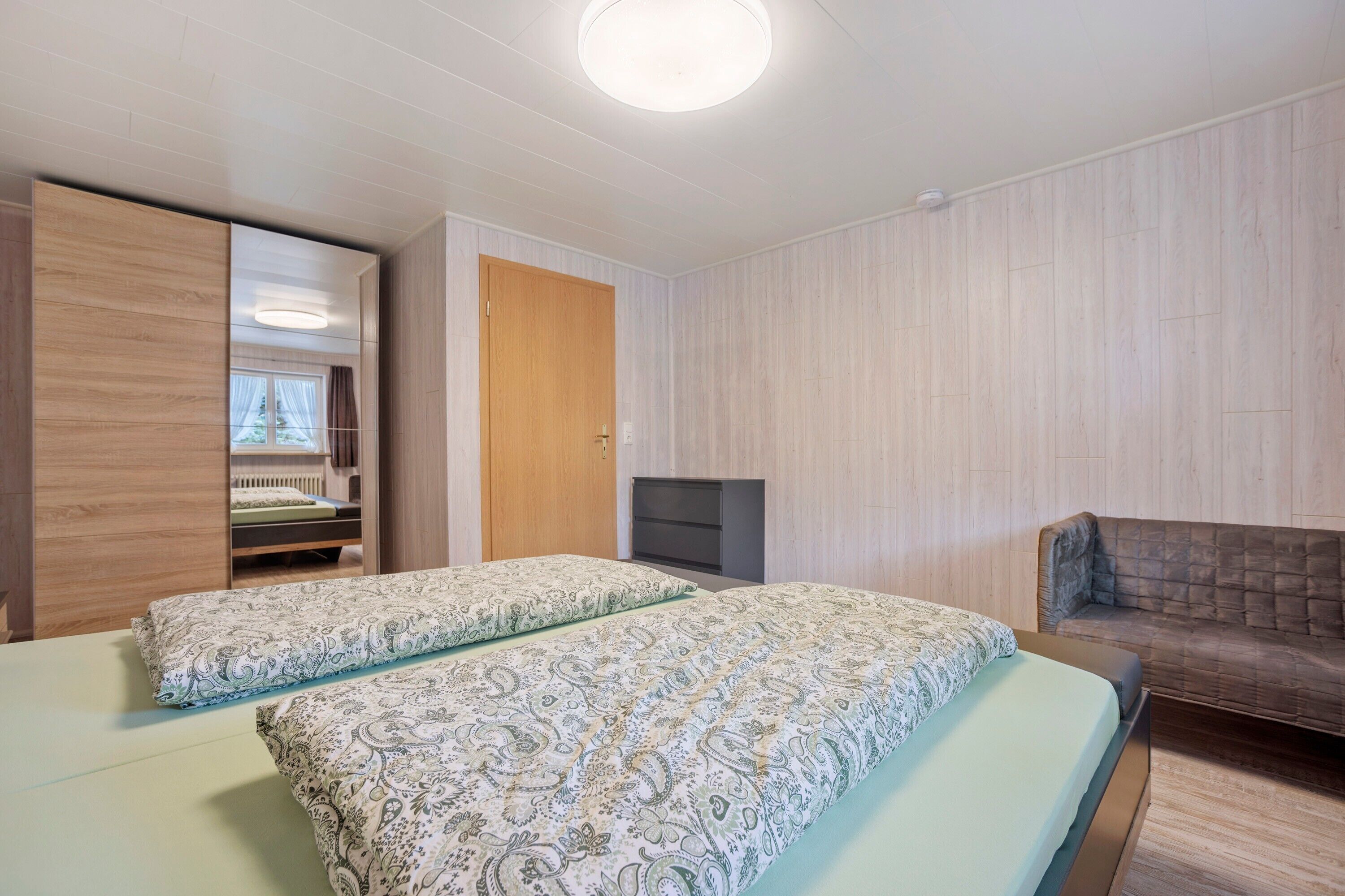 Een kamer met twee bedden, een houten garderobe, een televisie en een bank.