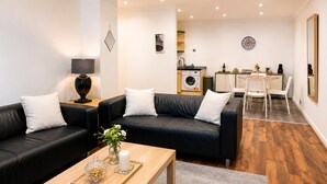 Ein modernes Wohnzimmer mit einem schwarzen Ledersofa, einem Holztisch und einem Essbereich mit weißem Tisch und Stühlen.