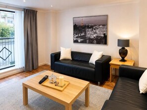 Un salon moderne avec un canapé en cuir noir, une table basse en bois, une télécommande, une bougie et une lampe.