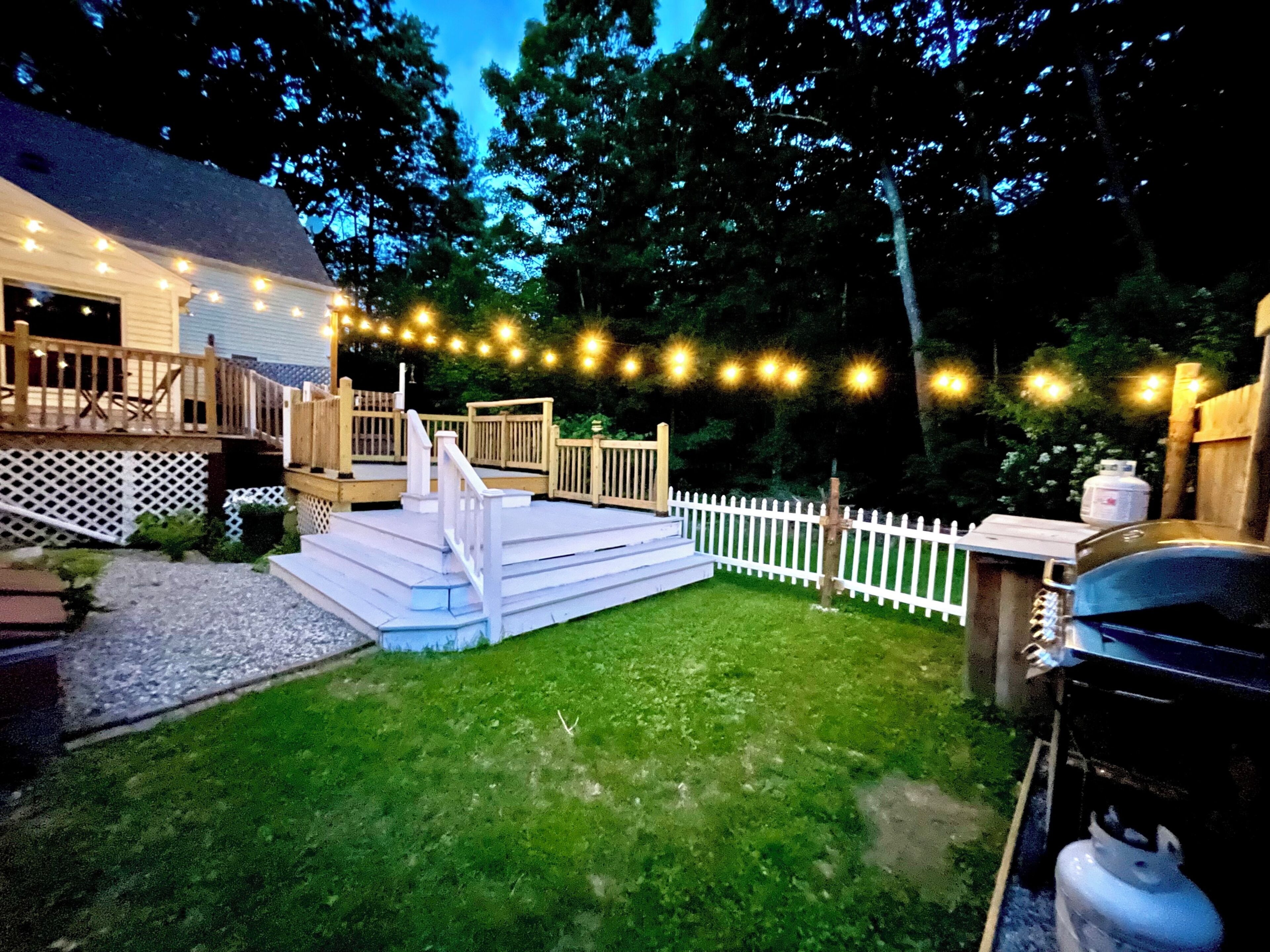 A backyard with a wooden deck, a white fence, and string lights.