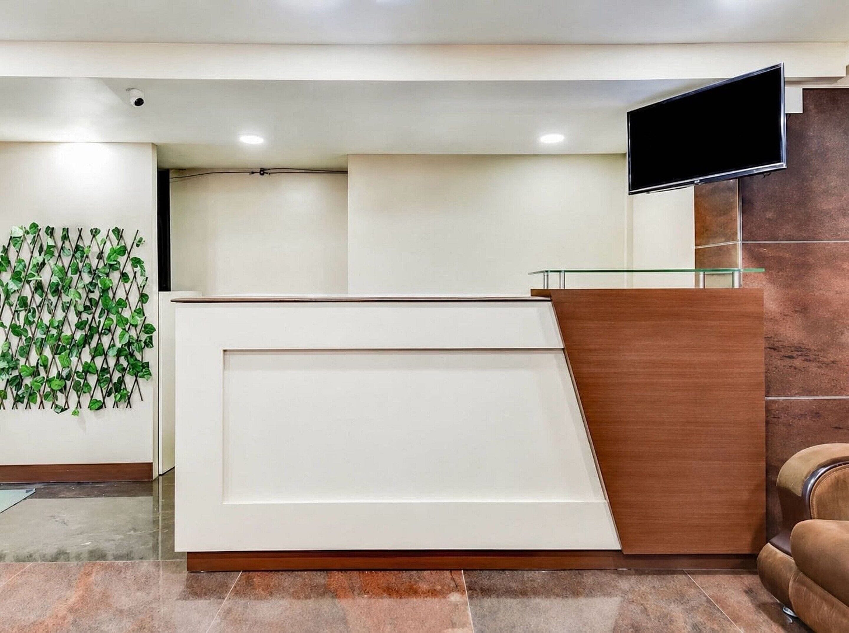 A reception desk with a flat-screen TV, a green plant wall, and a brown leather chair.