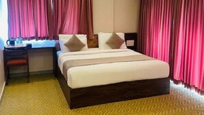 Hotellihuone, jossa on sänky, työpöytä ja verhot.