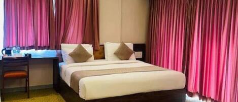 A hotel room with a bed, a desk with a chair, an air conditioner, and curtains.