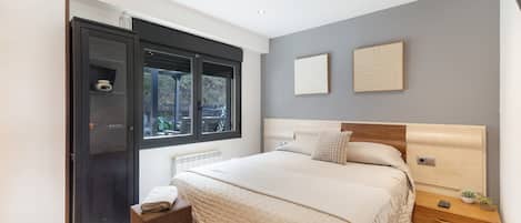 Un dormitorio moderno con una cama grande, un armario, un ventanal con vistas y una mesita de noche con una planta.