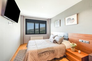 A modern bedroom with a large bed, a bedside table with a plant, and a view of the outdoors through a window. - Villa 'Ana Esperanza - El Espinar' with Lake Views, Wi-Fi, and Air Conditioning (El Espinar)