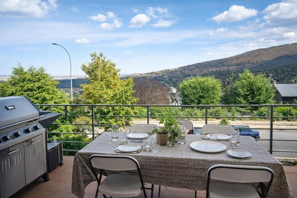 An outdoor dining area with a grill, table set for two, and a view of the surrounding landscape.