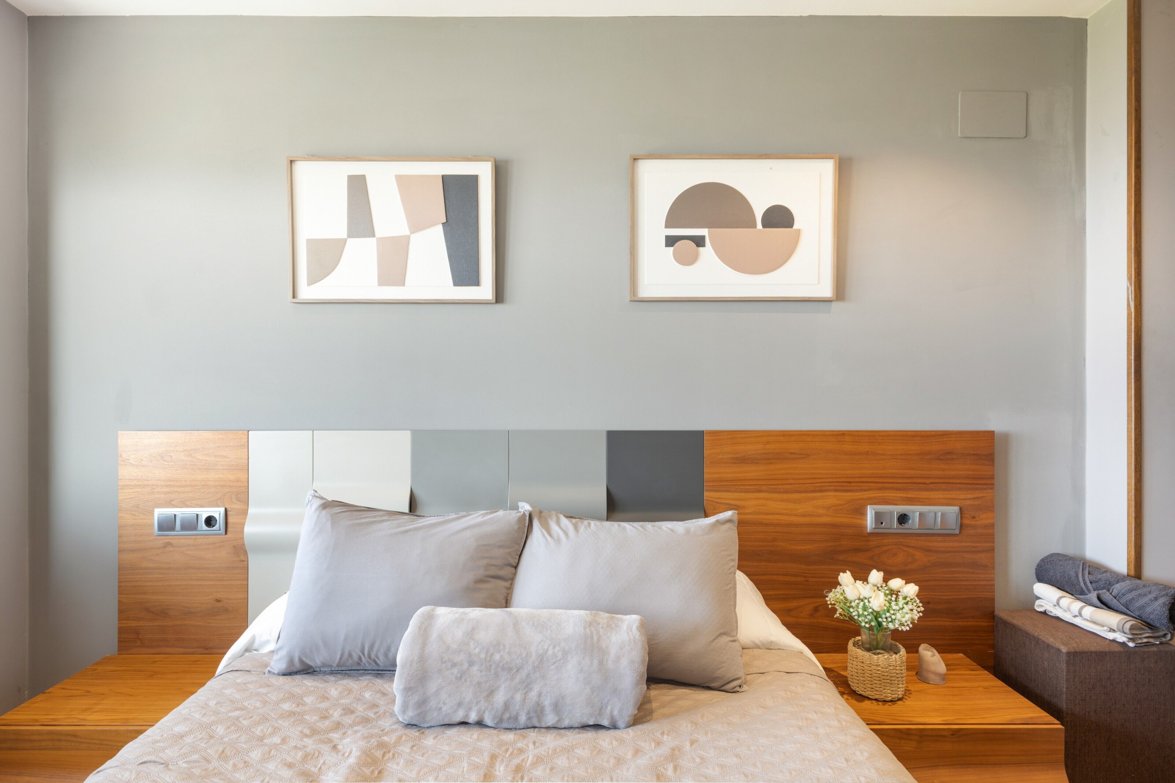 Une chambre à coucher avec un lit, des oreillers, une tête de lit, des tables de chevet et deux œuvres d’art abstraites encadrées accrochées au mur.