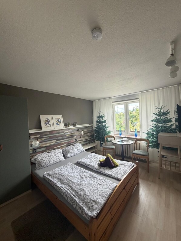 Ett sovrum med en säng, ett litet bord, stolar, ett element och ett fönster med gardiner.
