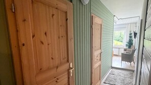 Un pasillo con puertas de madera, una pared verde y vistas a un espacio exterior con una silla y un árbol de Navidad.