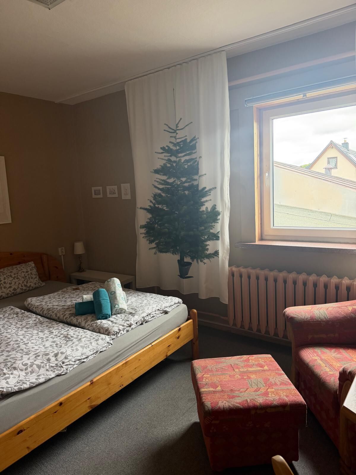 A room with two beds, a window with a view, a radiator, and a potted tree.