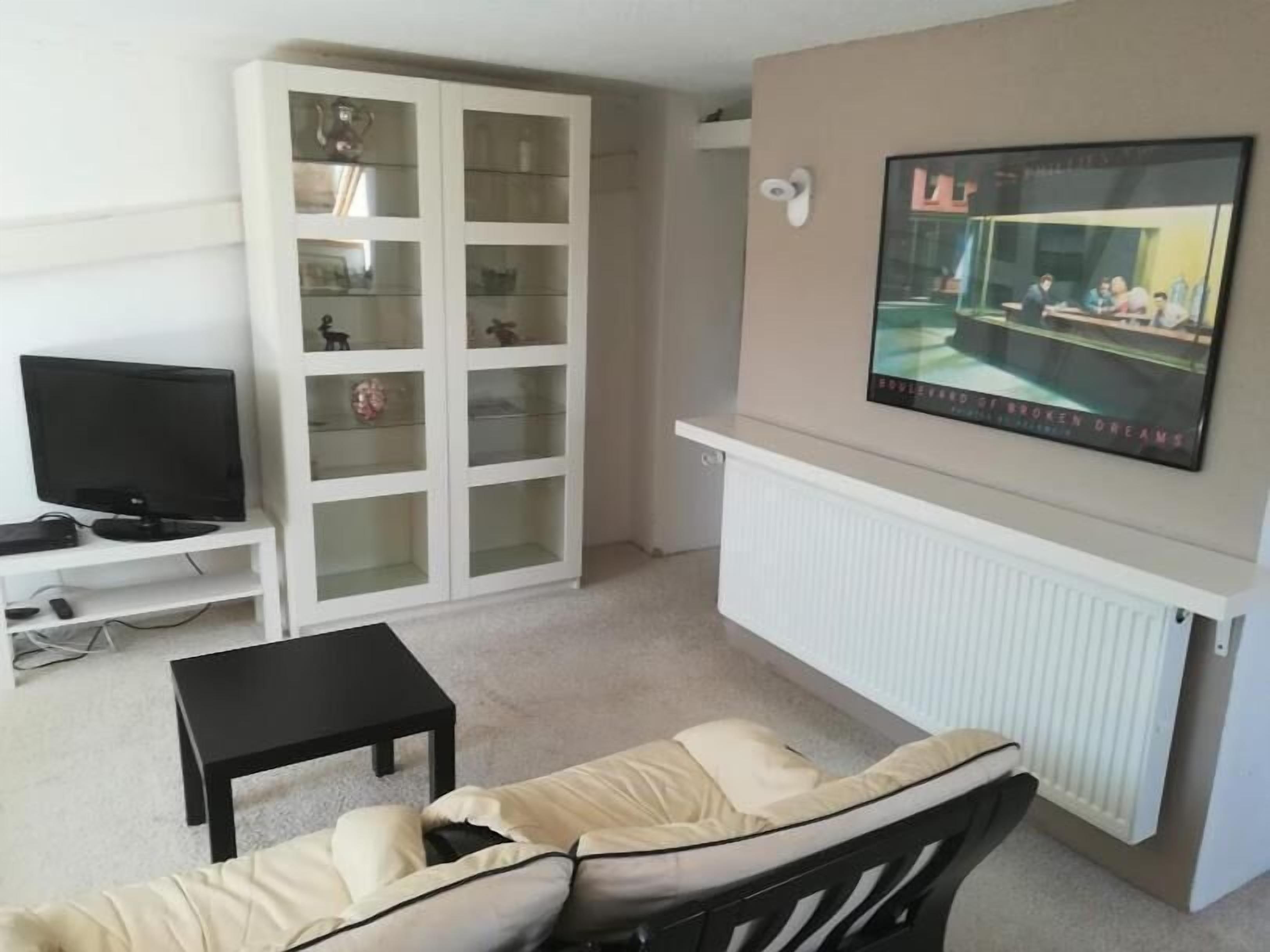 Una sala de estar con televisor, un mueble, un sofá y un cartel en la pared.