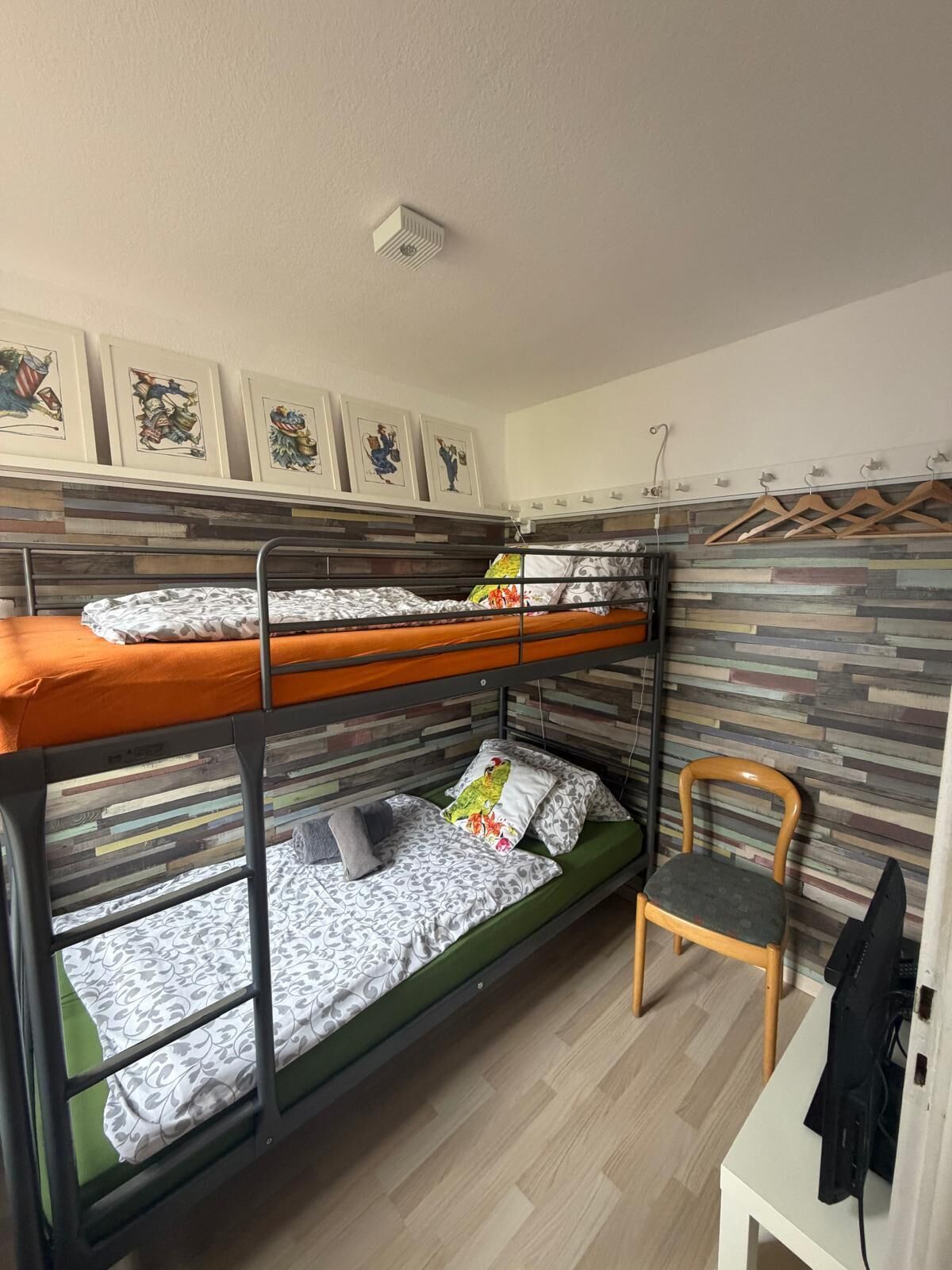 Habitación con literas, suelo de madera, una silla, una mesa y una pared con diseño a rayas.