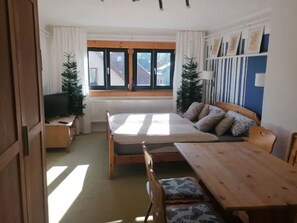 A room with a bed, a wooden table, a TV, and a window with curtains.