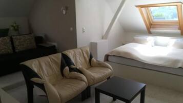 A loft-style bedroom with a sloped ceiling, a bed, a window with a view, a sofa, and a small table.