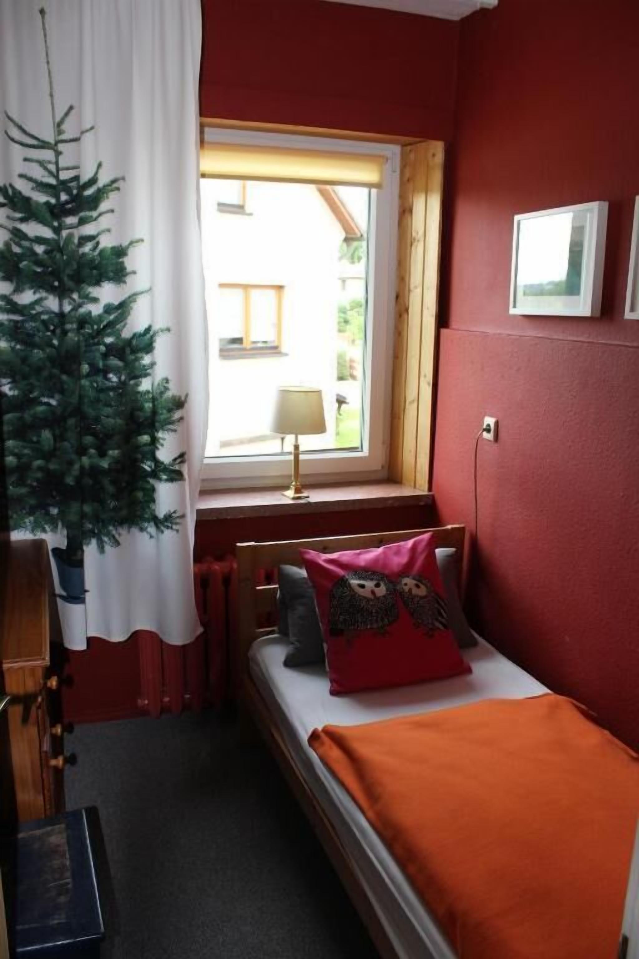A small room with a bed, a window with a view, a radiator, and a plant.