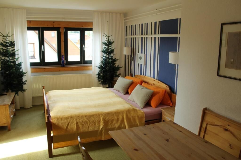 Un dormitorio con cama, sofá, mesa y ventana con cortinas.