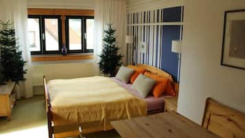 Un dormitorio con cama, sofá, mesa y ventana con cortinas.